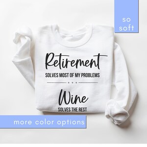 May include: White sweatshirt featuring the text "Retirement solves most of my problems. Wine solves the rest" in black. The words "so soft" and "more colour options" are also visible.