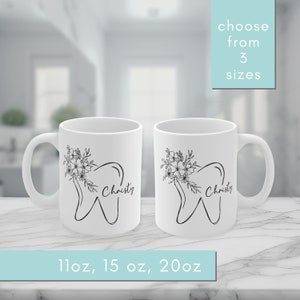Peut inclure: Deux tasses en céramique blanche avec des contours noirs d'une dent et un motif floral. Le texte "Christy" est écrit sur chaque tasse. Les tasses sont disponibles en tailles 11oz, 15oz et 20oz.