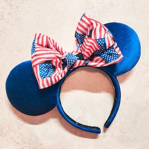 May include: Blue and red fabric headband with a bow featuring a red, white, and blue American flag pattern.