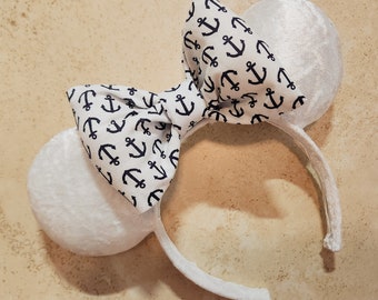 Könnte beinhalten: Weiße Mäuseohren mit einer weißen Schleife mit einem marineblauen Ankerdruck.