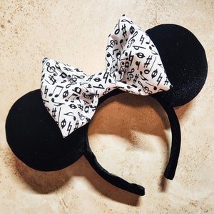 May include: Black velvet mouse ears with a white bow featuring a black musical note pattern.