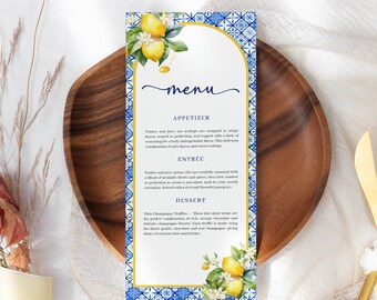Puede incluir: Una tarjeta de menú de azulejos azules y blancos con un borde dorado. La tarjeta de menú presenta una ilustración de acuarela de limones y flores. El menú incluye aperitivos, platos principales y postres. El texto en la tarjeta de menú dice "menú", "aperitivo", "plato principal" y "postre".