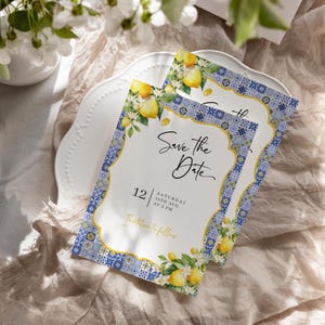 May include: Two "Save the Date" cards with a lemon and floral design. The cards have a white background with a blue and gold border. The text "Save the Date" is written in a script font. The date is August 12th.