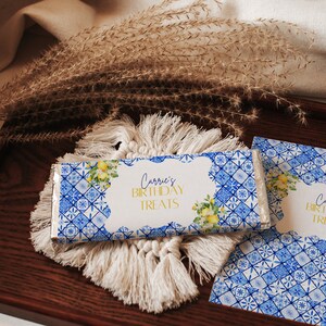 Könnte beinhalten: Ein blauer und weißer Schokoladenriegel-Wrapper mit einem weißen Etikett, auf dem "Carrie's Birthday Treats" steht. Der Wrapper zeigt ein florales Design mit Zitronen und Blättern.