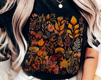 Puede incluir: Camiseta negra con un estampado floral colorido que presenta hojas, flores y tallos en tonos amarillos, naranjas, rojos y verdes.