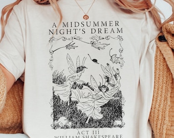 May include: Cream-colored t-shirt featuring a black and white illustration from Shakespeare's "A Midsummer Night's Dream." The design includes the title, a framed image of fairies, and the text "Act III, William Shakespeare."