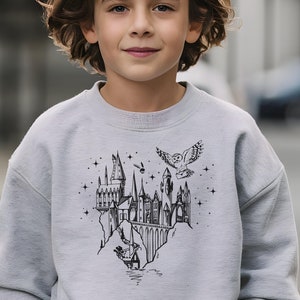 May include: A gray sweatshirt with a black and white graphic print of Hogwarts castle, a flying owl, and stars.