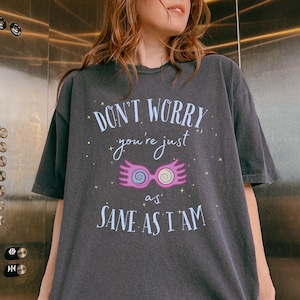 May include: A dark gray t-shirt with a graphic print of a pair of glasses with wings and the text "Don't worry, you're just as sane as I am."