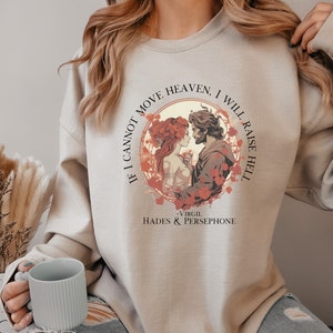 K&ouml;nnte beinhalten: Ein hellbeiger Pullover mit einem grafischen Druck eines Paares in einem Kreis. Der Text um den Kreis herum lautet "Wenn ich den Himmel nicht bewegen kann, werde ich die H&ouml;lle erheben - Virgil Hades & Persephone".