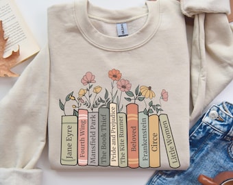 May include: A beige sweatshirt with a graphic of a stack of books with floral accents. The book titles include "Jane Eyre", "Fourth Wing", "Mansfield Park", "The Book Thief", "Pride and Prejudice", "The Kite Runner", "Beloved", "Frankenstein", "Circe", and "Little Women".