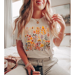 May include: White t-shirt with a colorful floral print featuring yellow, orange, red, and green flowers and leaves.