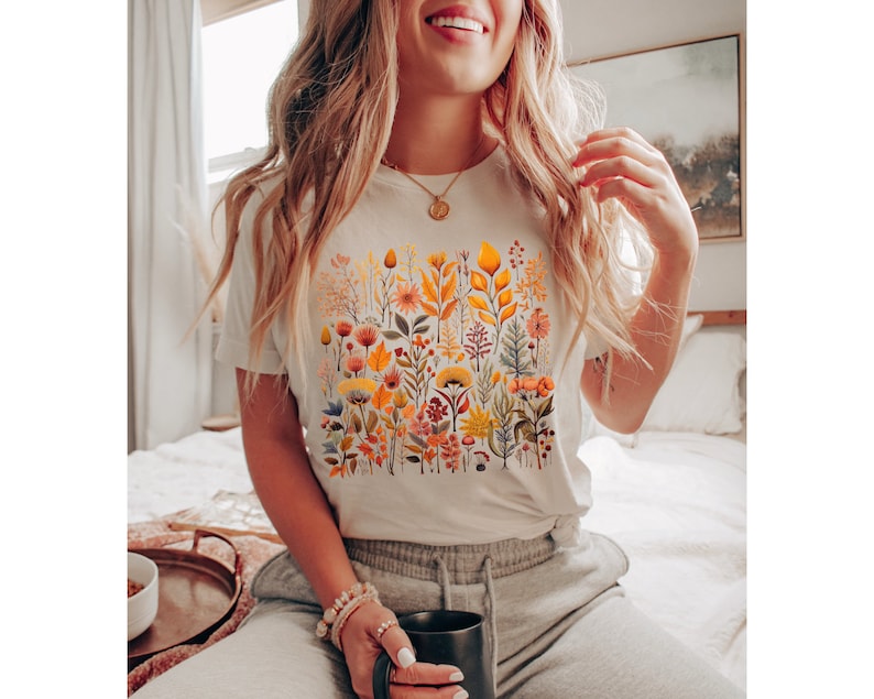 May include: White t-shirt with a colorful floral print featuring yellow, orange, red, and green flowers and leaves.