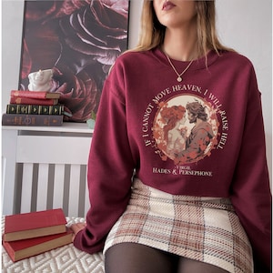 K&ouml;nnte beinhalten: Burgunderfarbener Pullover mit einem Grafikdruck von Hades und Persephone. Der Druck zeigt ein Zitat von Virgil: "Wenn ich den Himmel nicht bewegen kann, werde ich die H&ouml;lle entfachen."