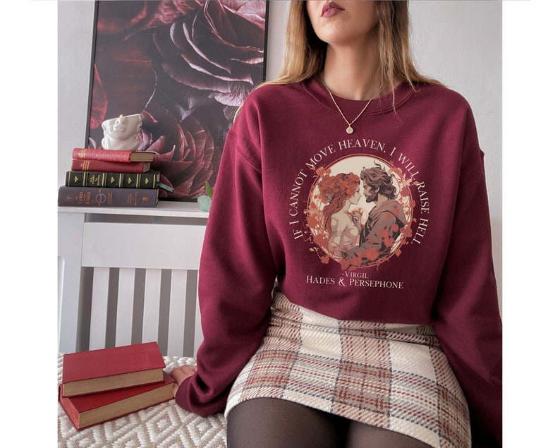 K&ouml;nnte beinhalten: Burgunderfarbener Pullover mit einem Grafikdruck von Hades und Persephone. Der Druck zeigt ein Zitat von Virgil: "Wenn ich den Himmel nicht bewegen kann, werde ich die H&ouml;lle entfachen."