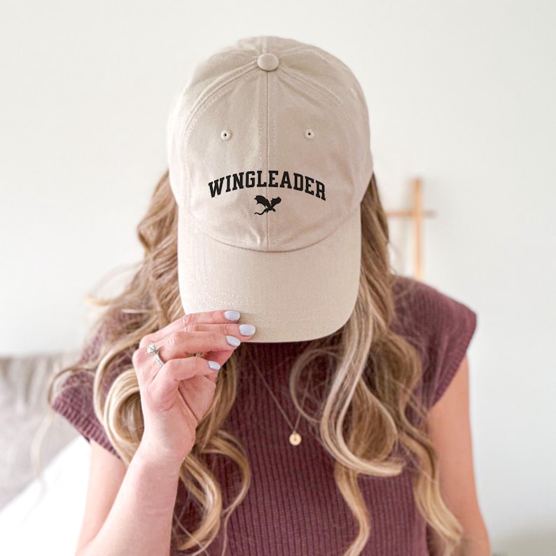 May include: A beige baseball cap with a black embroidered dragon and the text "WINGLEADER" on the front.