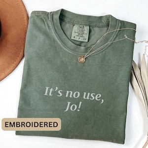 May include: A green t-shirt with the text "It's no use, Jo!" embroidered on the front. The shirt is made of a soft, comfortable fabric and has a relaxed fit.