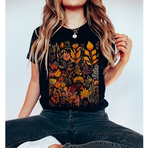 May include: A black t-shirt with a colorful floral print featuring a variety of flowers, leaves, and stems in shades of orange, yellow, and pink.