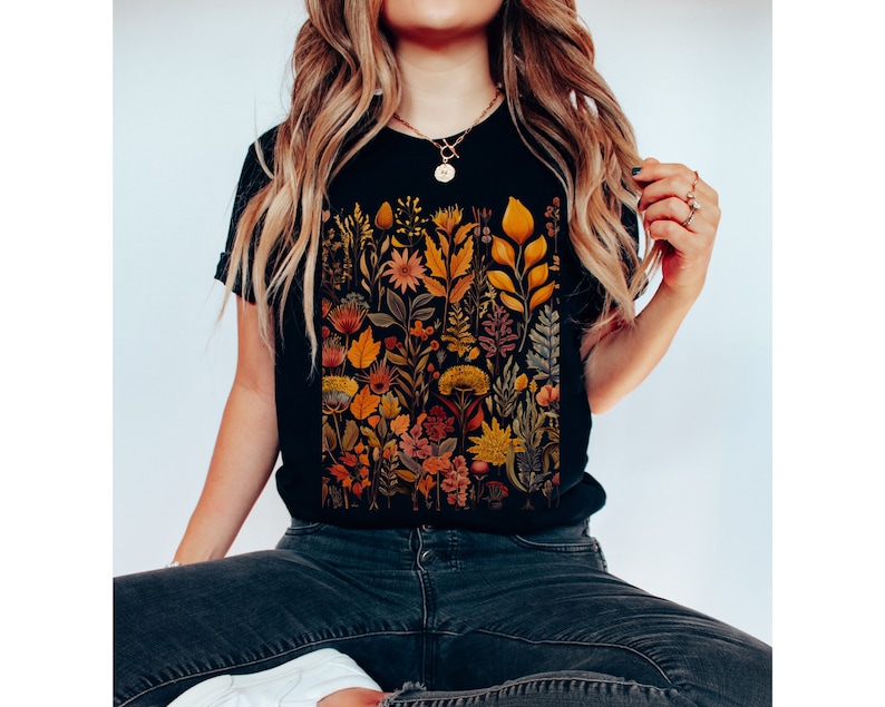 May include: A black t-shirt with a colorful floral print featuring a variety of flowers, leaves, and stems in shades of orange, yellow, and pink.