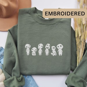 May include: A green sweatshirt with white embroidered characters from the movie 'My Neighbor Totoro'. The text 'EMBROIDERED' is in the top right corner of the image.