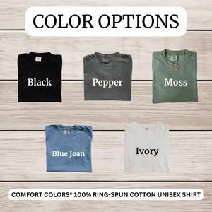 Op de afbeelding: Een display van vijf Comfort Colors unisex shirts in verschillende kleuren: zwart, peper, mos, spijkerbroekblauw en ivoor. De tekst "COLOR OPTIONS" staat bovenaan, met de kleuren van de shirts eronder. De onderste tekst luidt "COMFORT COLORS&reg; 100% RING-SPUN COTTON UNISEX SHIRT."