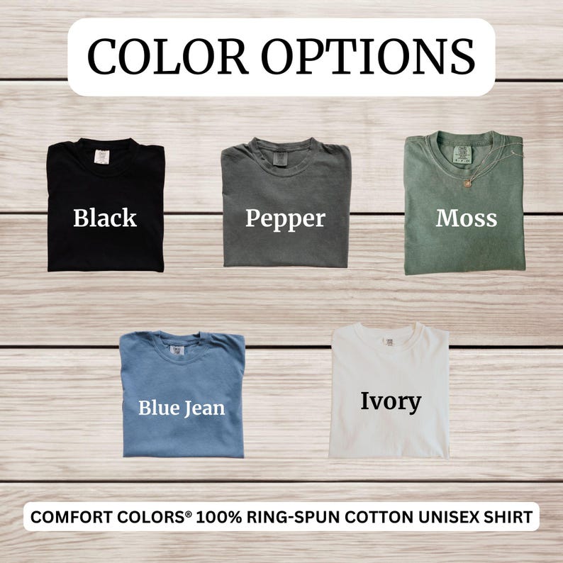 Op de afbeelding: Een display van vijf Comfort Colors unisex shirts in verschillende kleuren: zwart, peper, mos, spijkerbroekblauw en ivoor. De tekst "COLOR OPTIONS" staat bovenaan, met de kleuren van de shirts eronder. De onderste tekst luidt "COMFORT COLORS&reg; 100% RING-SPUN COTTON UNISEX SHIRT."