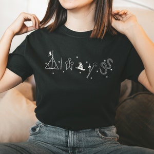 Może przedstawiać: Czarny t-shirt z białymi ikonami graficznymi i napisem "Always". Projekt zawiera symbol Insygniów Śmierci, piłki do Quidditcha, tiarę, różdżkę i węża. Koszulka wykonana jest z miękkiego materiału.