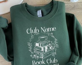 May include: A dark green sweatshirt with a white graphic design for a book club. The design includes a stack of books, a teacup, and floral elements, with the text "Club Name" and "Book Club Est. 2024".