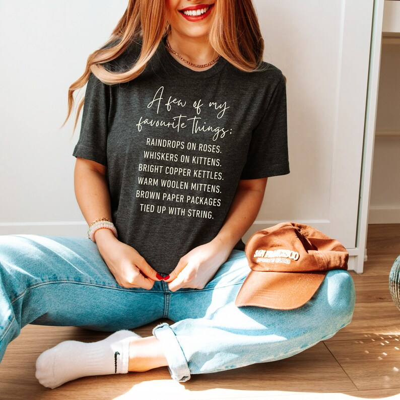 Puede incluir: Una camiseta gris oscuro con texto blanco que dice "A few of my favorite things: Raindrops on roses. Whiskers on kittens. Bright copper kettles. Warm woolen mittens. Brown paper packages tied up with string."
