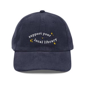 Peut inclure: Casquette de baseball en velours côtelé bleu marine avec l'inscription brodée "support your local library" en blanc, ornée d'étoiles jaunes. La casquette a une visière incurvée et une conception classique à six panneaux.