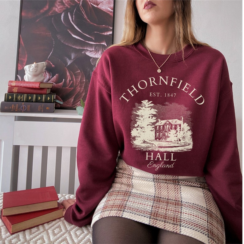 May include: A maroon sweatshirt with a white graphic print of a house with the text "Thornfield Hall, Est. 1847, England".