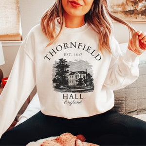 May include: White sweatshirt with a black graphic print of a house with the text "Thornfield Hall, Est. 1847, England"