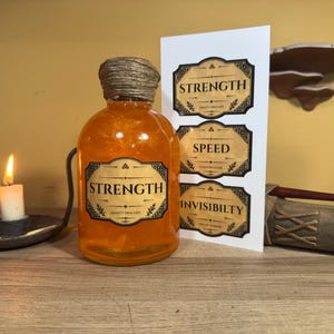 May include: A clear glass bottle filled with shimmering orange liquid, topped with twine, and labeled STRENGTH. Beside it is a white card with three labels: STRENGTH, SPEED, and INVISIBILTY. A lit candle in a dark metal holder sits to the left.
