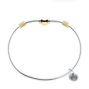 May include: A silver bangle bracelet featuring a central polished gold-tone bead, two textured gold-tone accents on either side, and a small circular silver charm dangling from the band, which is engraved with a simple line drawing of a sunset.