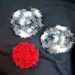 May include: Three crocheted scrubbers, one red, two black and white. The scrubbers are made with a fluffy yarn and have a round shape.