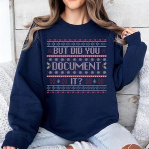 May include: Navy blue sweatshirt with a festive pattern and the text "BUT DID YOU DOCUMENT IT?". The design includes snowflakes and geometric shapes in red, white, and blue. The sweatshirt is a comfortable, casual garment.