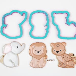 Puede incluir: Un juego de cuatro cortadores de galletas, con un elefante, un le&oacute;n, un tigre y un conjunto de tres galletas de animales. Los cortadores de galletas son de color azul turquesa con letras moradas. Las galletas est&aacute;n decoradas con glaseado y presentan un elefante, un le&oacute;n y un leopardo.