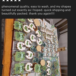 May include: A display of decorated sugar cookies, featuring golf course and baby bib designs. The cookies are iced in green, white, and beige, and arranged on wire racks. Some cookies have the text "Best Dad by Par".