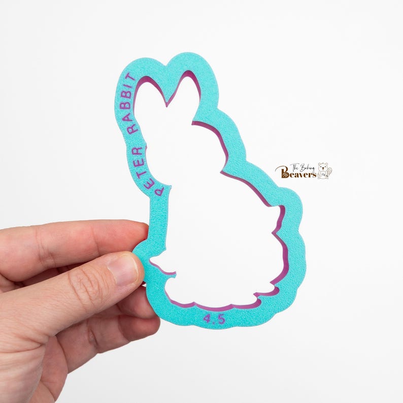 May include: A teal and purple Peter Rabbit cookie cutter. The text "PETER RABBIT" is printed in purple along the side of the cutter. The number "4.5" is printed in teal at the bottom. The Baking Beavers logo is in the upper right corner.