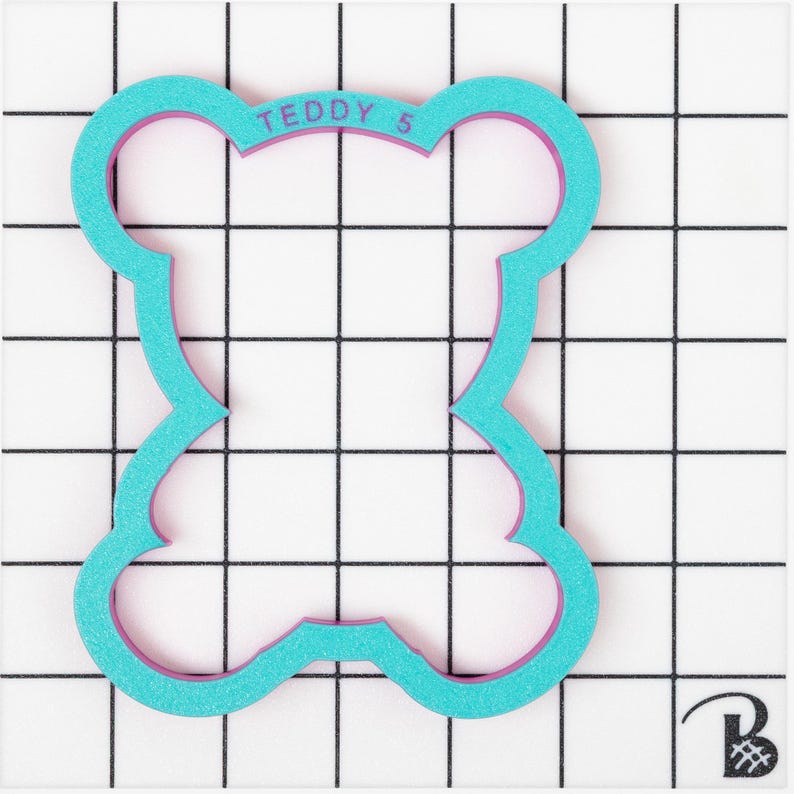 May include: A turquoise blue cookie cutter shaped like a teddy bear with a pink outline. The cookie cutter has the text "TEDDY 5" on the top.
