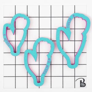 Op de afbeelding: Drie turquoise blauwe plastic koekjesvormen in de vorm van tulpen. De vormen zijn gelabeld "TULIP 3", "TULIP 3.5" en "TULIP 4".