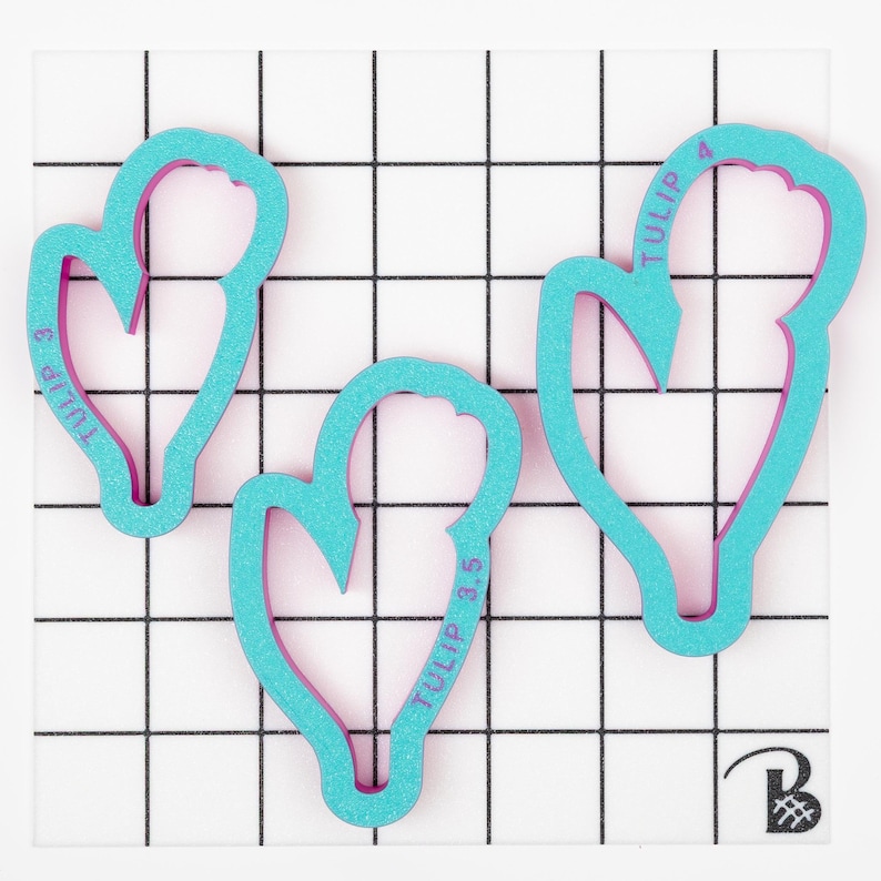 Op de afbeelding: Drie turquoise blauwe plastic koekjesvormen in de vorm van tulpen. De vormen zijn gelabeld "TULIP 3", "TULIP 3.5" en "TULIP 4".