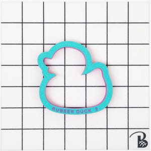 May include: A turquoise blue rubber duck cookie cutter with a pink outline. The cutter has the text "Rubber Duck 3" on the bottom.
