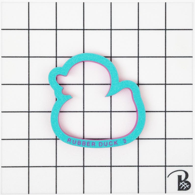 May include: A turquoise blue rubber duck cookie cutter with a pink outline. The cutter has the text "Rubber Duck 3" on the bottom.