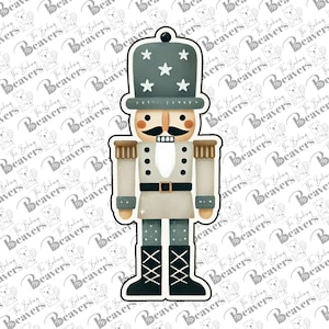 May include: A gray and white nutcracker cookie cutter with a blue hat and a black belt. The cookie cutter is in the shape of a traditional nutcracker with a mustache and a beard.