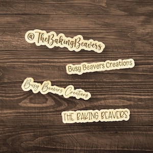 May include: Four wooden signs with different variations of the text "The Baking Beavers" and "Busy Beavers Creations". The signs are on a brown wooden background.