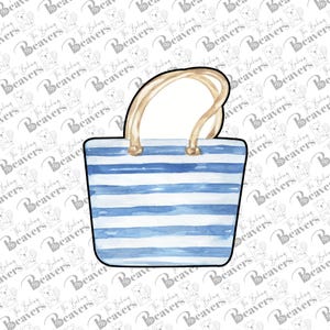 May include: A beach bag cookie cutter with a blue and white striped design. The bag has a tan handle and gold-colored accents. The cutter is made of metal and is ideal for making cookies for a summer-themed event.