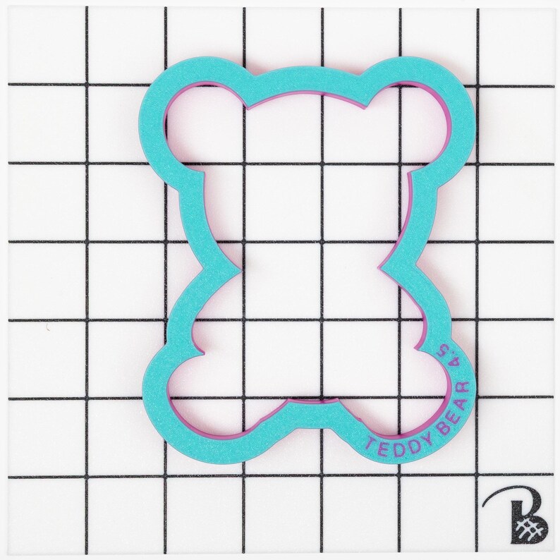 May include: A turquoise blue cookie cutter shaped like a teddy bear with a pink outline. The cutter has the words "Teddy Bear 4.5" printed on the bottom.