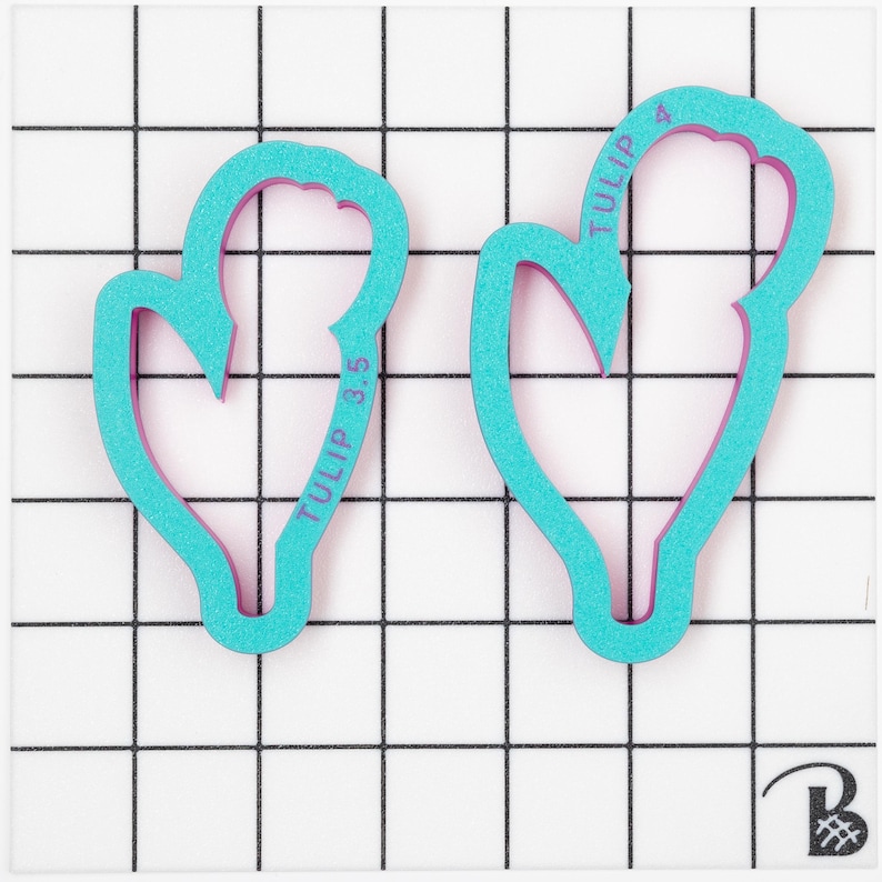 Op de afbeelding: Twee tulpenvormige koekjesvormen in turquoise blauw. De grotere vorm heeft de tekst "TULIP 4" erop gedrukt. De kleinere vorm heeft de tekst "TULIP 3.5" erop gedrukt.