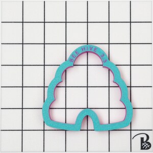 May include: A teal bee hive shaped cookie cutter with a purple interior. The text "BEE HIVE 35" is printed on the top arch of the cutter. The cutter is on a white surface with a black grid pattern.