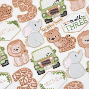 Puede incluir: Un conjunto de galletas de az&uacute;car decoradas con un tema de selva. Las galletas est&aacute;n decoradas con varios animales, incluyendo un le&oacute;n, un elefante, una jirafa y un leopardo. Las galletas tambi&eacute;n presentan los n&uacute;meros 3 y las palabras "You're Wild Three" y "Matthew".
